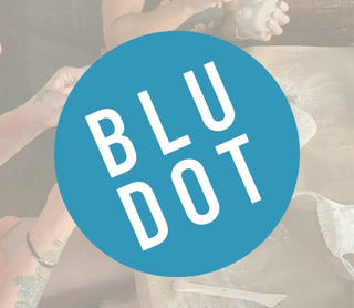 Blu Dot logo with a blurred background of people and clay