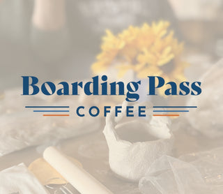 Boarding Pass Coffee logo with a blurred background of a ceramic pot and flowers.