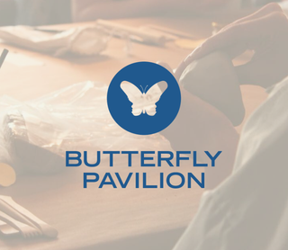 A blue circular logo with a white butterfly and the text 'BUTTERFLY PAVILION' overlaid on a softly blurred indoor scene with warm lighting and a person seated at a table.