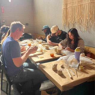 Group of people sitting at a table making pottery in a workshop.