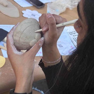 Person working on a small clay sculpture with a wooden tool