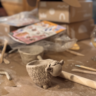 Clay sculpture of a sheep on a worktable with pottery tools and materials.