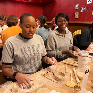 Two women sitting at a table in a red-walled room, engaged in a craft activity.