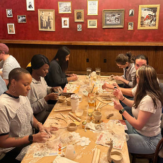 Group of people sitting around a table making pottery in a workshop.