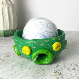 Green yarn bowl that looks like a fish  with a ball of yarn on a textured surface