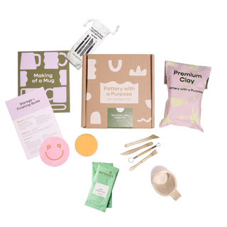 Pottery-making mug kit with clay, tools, and instructions on a white background