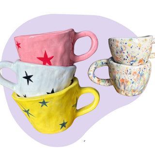 Colorful ceramic mugs with star and floral patterns on a light purple background