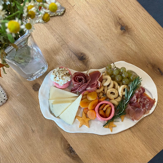Platter of assorted meats, cheeses, and fruits on a wooden table with flowers in the background.