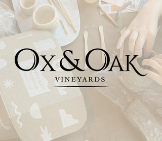 Ox & Oak Vineyards branding with wine glasses and decorative elements on a blurred background of a pottery class table setting