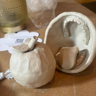 Clay pot with teeth and tongue and sculpture of an apple on a table