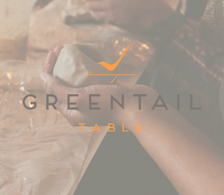A person's hands holding a light-colored piece of clay over a worktable, overlaid with the text 'GREENTAIL TABLE' and an orange logo.