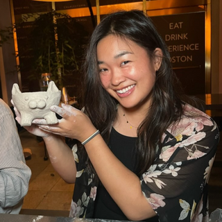Woman holding a small ceramic cat sculpture at a pottery class.