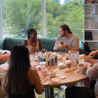 Group of people sitting around a table with coffee cups and snacks, surrounded by greenery.