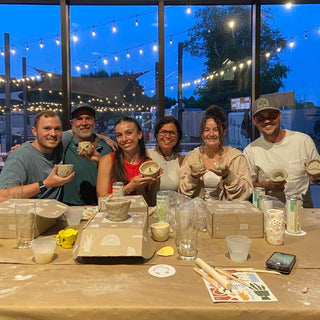 Group of people at a pottery studio with finished ceramic items and tools on a table.