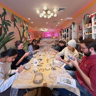 Group of people sculpting potter around a table in a colorful room with shelves and decor.
