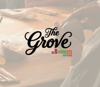 A warm-toned lifestyle scene showing a person holding a white mug at a wooden table, with the overlaid text 'The Grove at the Lawn on D' in black and small colored blocks.