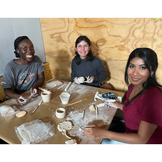 Three women sitting at a table making pottery in a workshop.