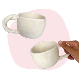 White ceramic mugs with braided handle held by a hand on a pink background