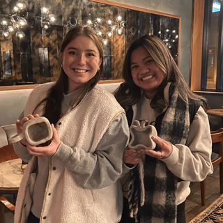 Two women holding small pottery pices in a cozy indoor setting.