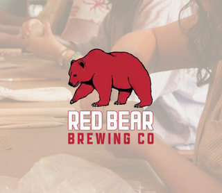 A faded background photo of people at a table, overlaid with a prominent red bear logo and the text 'RED BEAR BREWING CO' in white and red.
