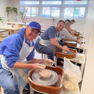 People working with clay on pottery wheels in a classroom setting.