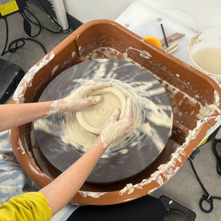 Person working with clay on a pottery wheel in a studio setting.