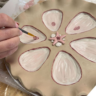 Hand painting a ceramic plate with shell designs and a starfish decoration.