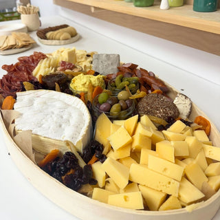 Assorted cheeses, meats, and olives on a wooden board at pottery studio.