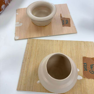 Two ceramic pots on wooden placemats with name tags.