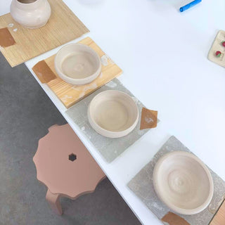 ceramic bowls on a white surface with a wooden stool and additional bowls in the background.