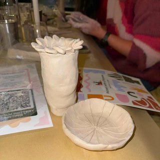 Two ceramic pieces on a table with a person working in the background