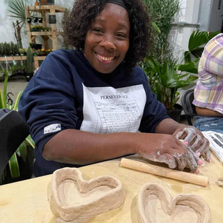 Person making heart-shaped dishes at a table with plants in the background