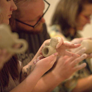 Person holding a clay pot with another person in the background