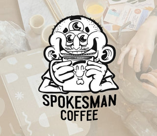 Spokesman Coffee logo with a cartoon character holding a coffee cup on a blurred background.