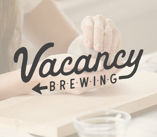 Person holding a mug with 'Vacancy Brewing' logo on a blurred background