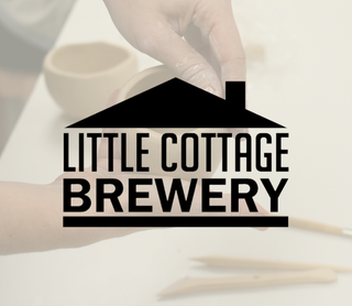 A hand holds a small beige ceramic mug over a white surface, with a large black 'LITTLE COTTAGE BREWERY' house logo overlaid across the center.