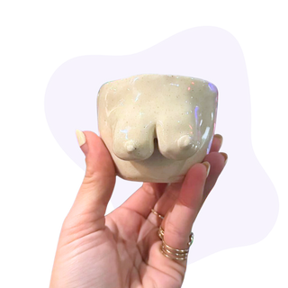 Hand holding a ceramic object shaped like a female torso against a white background