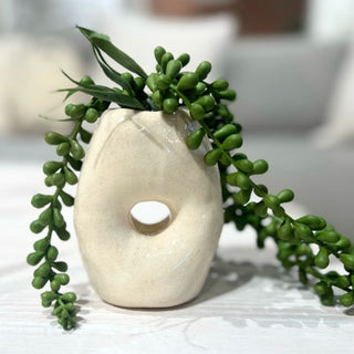 White donut-shaped vase with green plant on a light surface