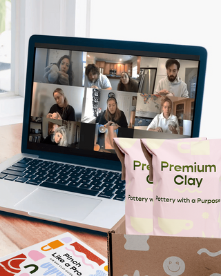 Laptop on a table displaying a video call with people doing pottery during a team event, next to a box with two bags labeled 'Premium Clay - Pottery with a Purpose' as well as a pamphlet that says 'Pinch Like a Pro - Air Dry Clay Guide'.