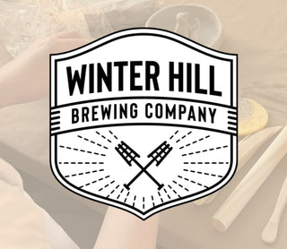 Winter Hill Brewing Company logo with crossed mugs on a blurred background